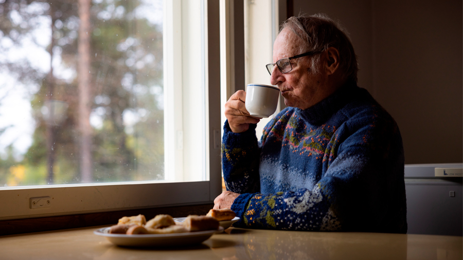 Seniori juo kahvia pöydän ääressä ja katselee ulos ikkunasta
